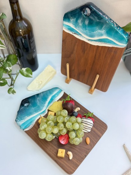 Handcrafted walnut charcuterie board with ocean wave resin design, styled with cheese, fruits, and nuts on a clean white background.